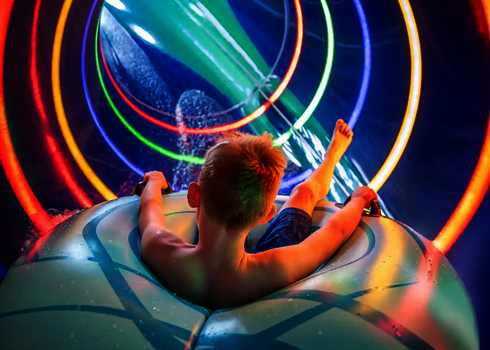 Kind sitzt in Rutschreifen in einer Röhrenrutsche mit bunten Lichtspielen.