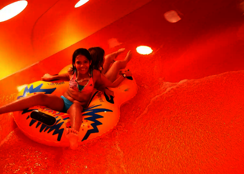 Zwei Kinder rutschen in einem Reifen durch eine Röhrenrutsche.