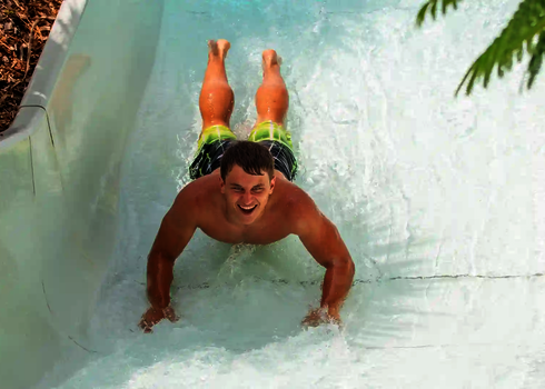 Ein Mann rutscht lachend bäuchlings durch einen Wildwasserfluss.