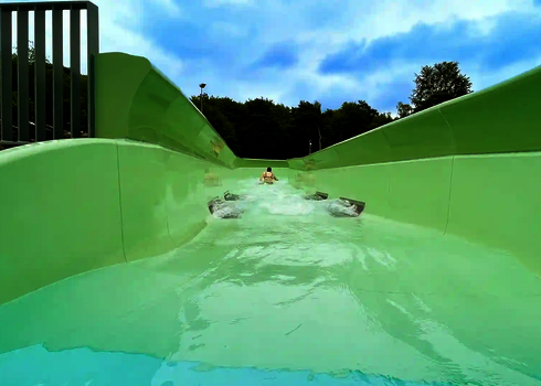 Eine Person rutscht bäuchlings durch den grünen Wildwasserfluss mit starker Strömung.