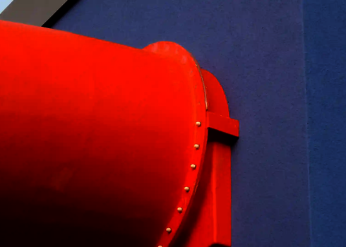 Orangefarbene Wasserrutsche tritt durch eine blaue Gebäudefassade ins Freie.