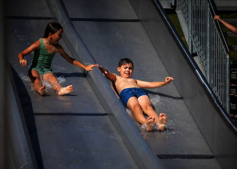 Mädchen und Junge geben sich auf der Trio-Slide rutschend die Hand.