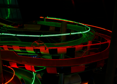 Komplexe Rutschlandschaft mit Body Racer Wasserrutschen, rot und grün leuchtend in der Dunkelheit.