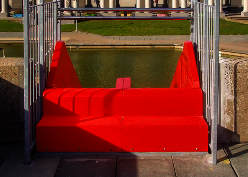 Startbereich einer roten Multilane im Freibad mit Geländer und Blick auf Wasserfläche.