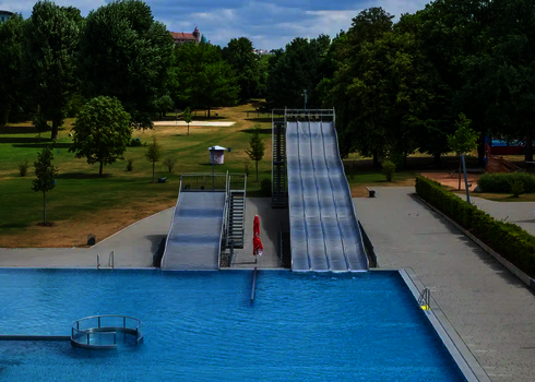 Eine Multilane und eine Breitwellenrutsche aus Edelstahl im Freibad mit Blick auf die große Liegewiese.