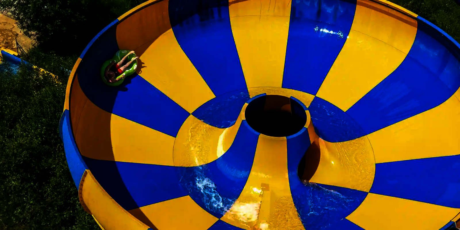 Gelb blaue Raft Bowl Reifenrutsche, Person rutscht auf grünem Rutschreifen.