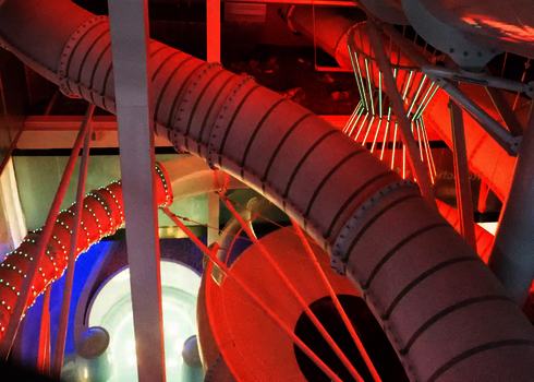 Mehrere mit LED-Lichteffekten versehene weiße Wasserrutschen, in orangefarbenen Licht.