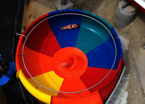 Bunte Body Bowl Wasserrutsche, in der eine Person mit Badekleidung rutscht.