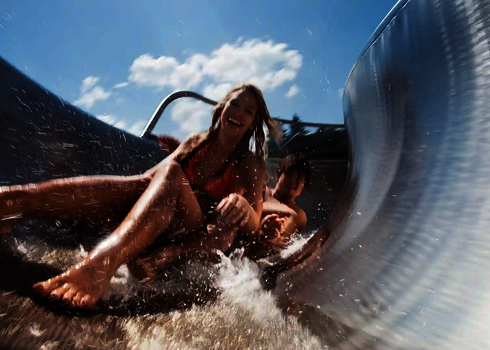 Zwei Personen rutschen lachend nebeneinander auf WR1040 mit spritzendem Wasser.
