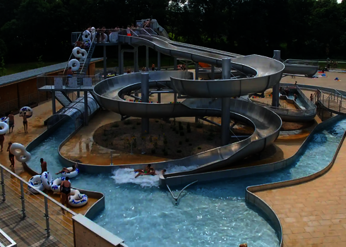 Wasserpark mit Edelstahlrutschen und vielen Badegästen mit Rutschreifen.