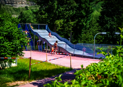 Ein rotes Absperrband in einem Freibad, im Hintergrund eine Breitwellenrutsche mit Badegästen.