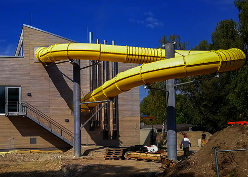 Eine gelbe RR1200 Wasserrutsche unter freiem Himmel, die in ein Gebäude führt.