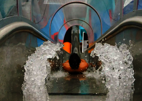 Rutschender Gast in startender Position in der transparenten Freifallrutsche mit Wasserstrahl.