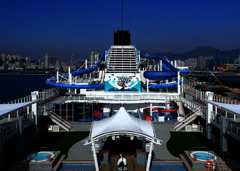 Kreuzfahrtschiffsdeck mit zwei blauen Wasserrutschen im Hintergrund.