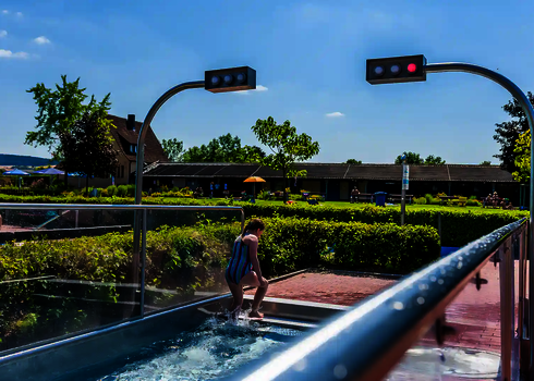 Kind verlässt den Auslaufbereich in einem Freibad über dem zwei Sensorampeln hängen.