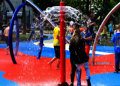 Personen unter Sprühsäule auf einem Wasserspielplatz.