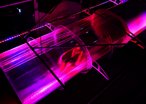 Indoor-Acrylröhre mit pink-violettem LED-Licht und rutschender Person im Wasserstrom.