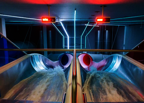 Blick auf die Raft Racer Reifenrutsche mit rot-blauen Röhren und Wasserzufluss bei LED-Licht.