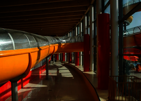 Innenansicht: Gelbe Wasserrutsche verläuft entlang der Glasfassade durch die Halle.
