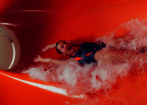 Innenansicht einer Wasserrutsche in der eine Person mit Badebekleidung rutscht.