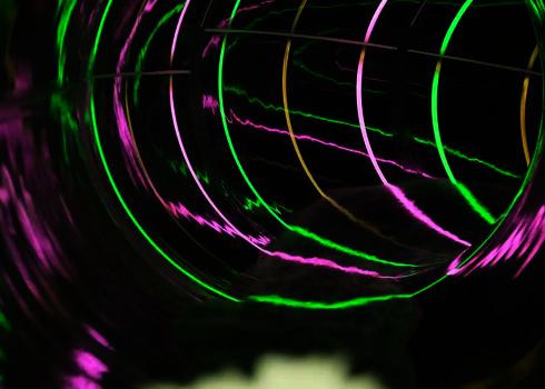 Innenansicht einer Wasserrutsche mit grünen und pinken Lichtstreifen im Dunkeln.