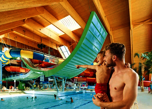 Vater mit Kind im Arm zeigt auf die große grüne Boomerang-Rutsche über dem Wasserbecken.