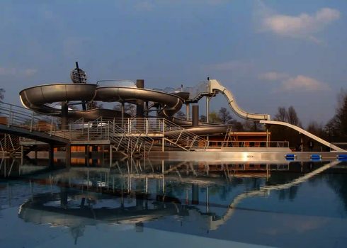 Wasseranlage mit Schwimmbecken und Edelstahlrutschen  im Hintergrund.