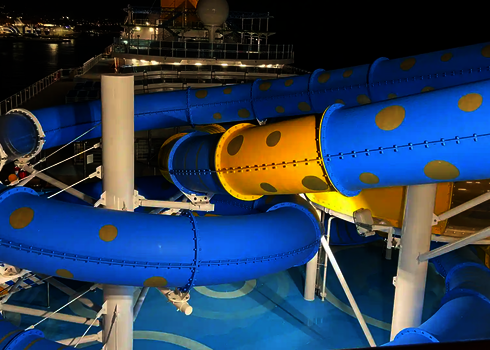 Eine blau und gelbe Röhrenrutsche mit Punkten auf einem Kreuzfahrtschiff bei Nacht.