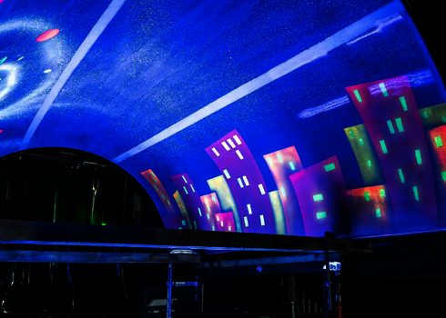 Bunte Häuser-Silhouetten und Sternenhimmel auf leuchtend blauer Röhreninnenfläche.