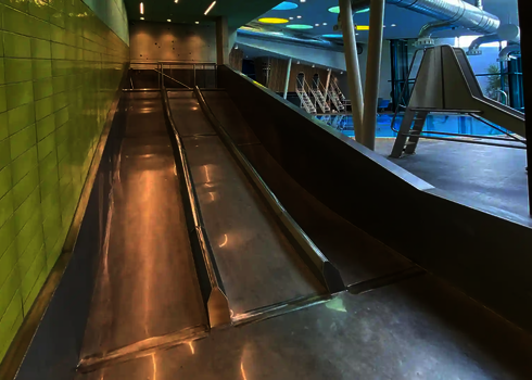 Trio-Slide im Innenbereich, daneben Schwimmbecken mit Sprungtürmen sichtbar.