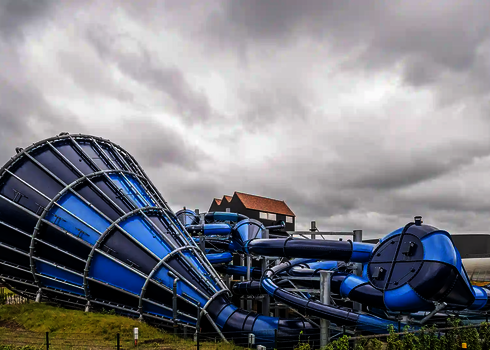 Blauer Cyclone-Trichter mit komplexer Röhrenrutsche vor grauem Himmel und Gebäuden.