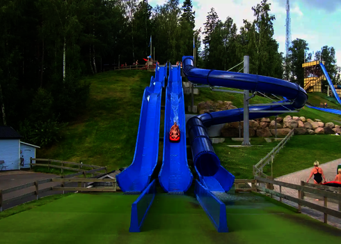 Blaue Harakiri Freizeitparkrutsche, die einen grünen hang hinabführt.