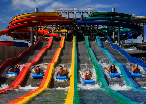 Sechs Personen auf blauen Rutschmatten rutsche eine bunte Matracer Wasserrutsche herunter.
