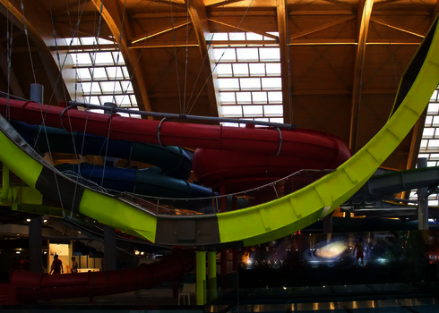 Indoor-Wasserrutschenanlage mit roten, grünen und gelben Wasserrutschen unter einem Holzdach.