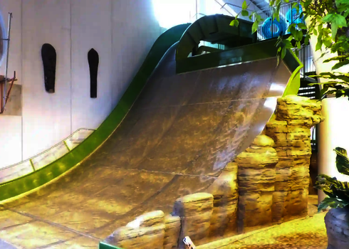 Indoor-Boomerang-Rutsche mit grüner Seitenverkleidung und Naturdeko.