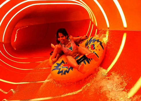 Mädchen rutscht lachend auf gelbem Reifen durch orangene Family Twister Wasserrutsche.