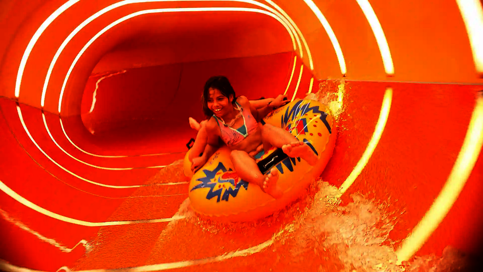 Mädchen rutscht lachend auf gelbem Reifen durch orangene Family Twister Wasserrutsche.