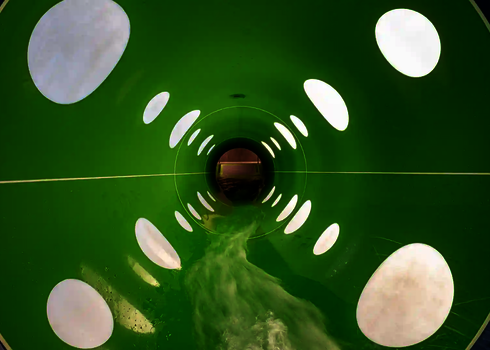 Innenansicht einer grünen Röhrenrutsche mit gepunkteten Tageslichteffekten.