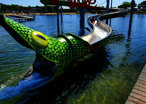 Snake-shaped slide with open mouth as a landing area directly into a lake.