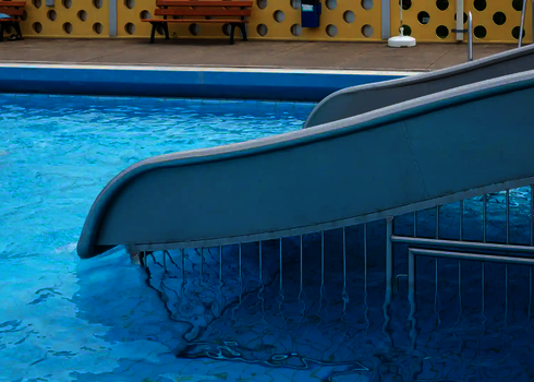 Eine Breitwellenrutsche mit einem Unterschwimmschutzgitter in einem blauen Schwimmbecken.