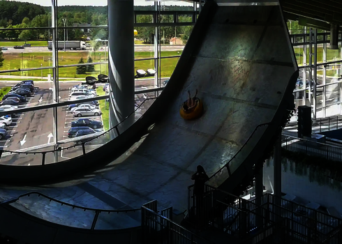 Person im gelben Rutschreifen auf der steilen Rampe der Boomerang-Rutsche mit Spritzschutz.