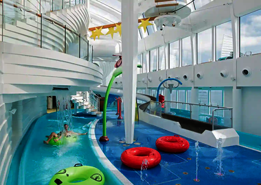Lazy River im Indoor Bereich eines Kreuzfahrtschiffes mit Rutschreifen, Wasserattraktionen und bunten Spielgeräten.