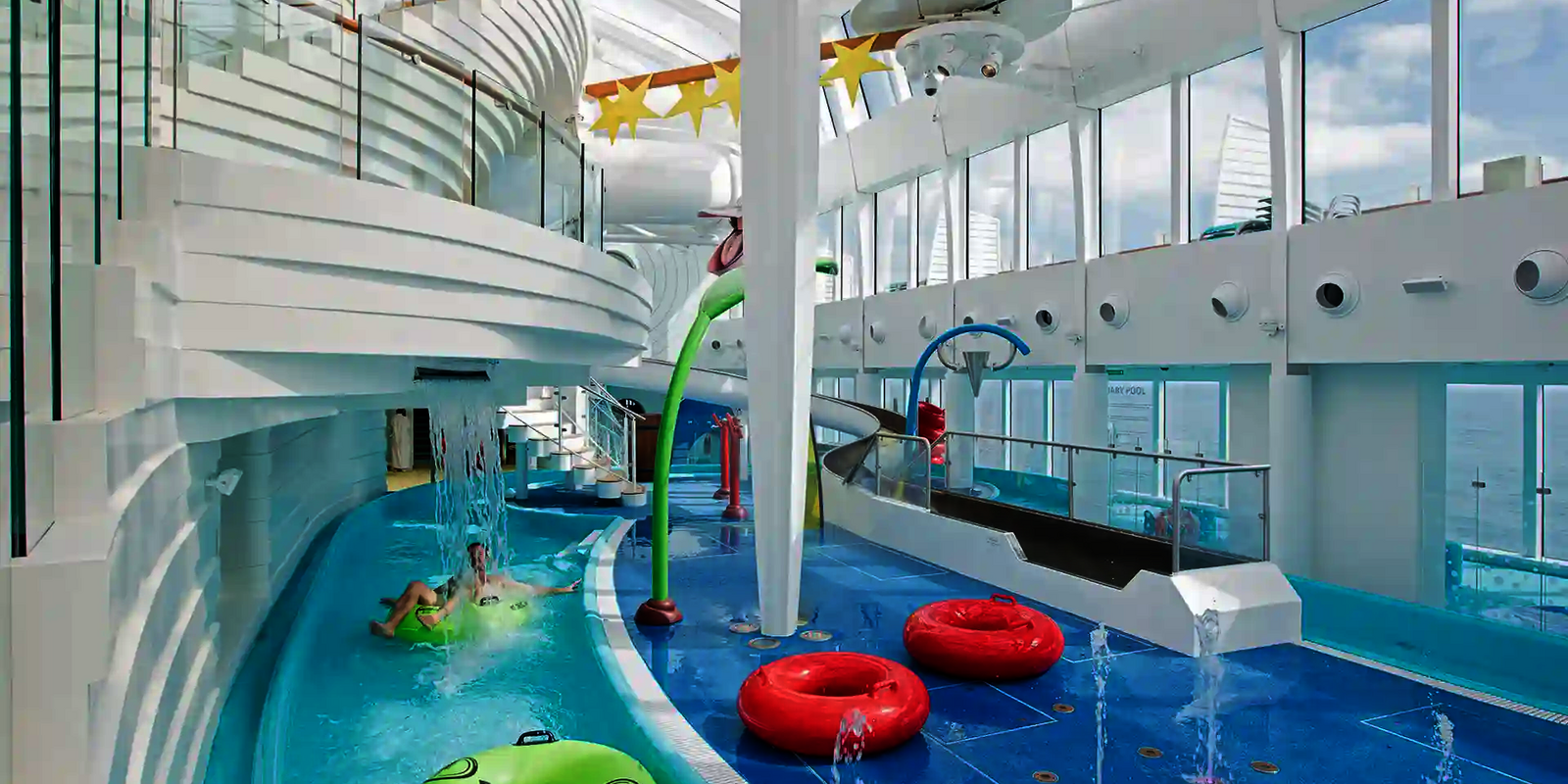 Lazy River im Indoor Bereich eines Kreuzfahrtschiffes mit Rutschreifen, Wasserattraktionen und bunten Spielgeräten.