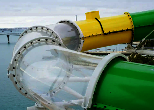 Nahaufnahme eines Übergangs von gelbem zu grünem Rutschenrohr mit klarem Acryl-Element über Wasser.