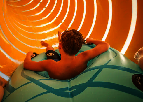 Ein Kind in einem blauen Rutschreifen in einer gelben Röhrenrutsche.