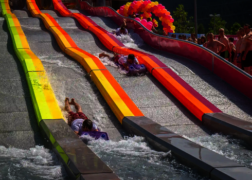 Personen rutschen auf bunten Matten nebeneinander die steile Wasserrutsche Matracer hinunter.