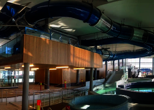 Blaue Wasserrutsche mit mehreren Acryl-Abschnitten in einem Hallenbad, von der Decke hängend.