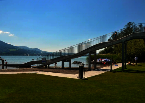Eine Breitwellenrutsche in einem Freibad, mit Blick auf die Berge und den See im Hintergrund.