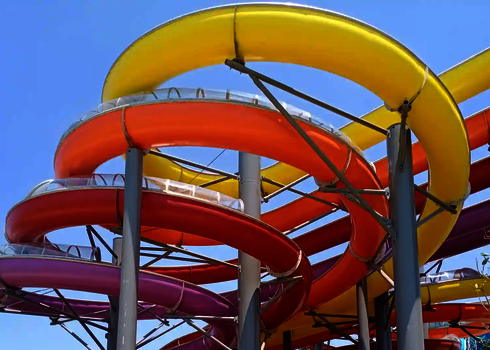 Blick von unten auf vier übereinanderliege bunte Kurvenabschnitte einer Wasserrutsche.