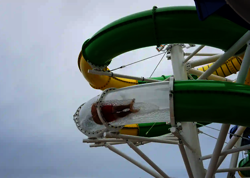 Eine Person rutscht durch ein Acryl-Stück, umgeben von grün-gelben Rutschenrohren in luftiger Höhe.